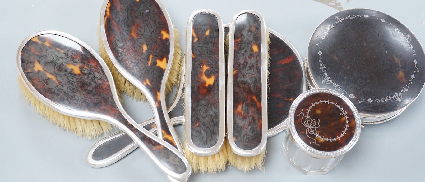 A George V matched silver and tortoiseshell mounted five piece mirror and brush set, a George V silver and tortoiseshell pique mounted circular box with mirrored interior and a similar mounted glass toilet jar.